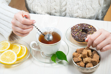 A woman in a large knit sweater holds a cup of hot tea in her hands. Hands close-up.