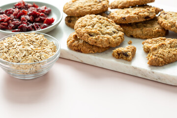 Close view of oatmeal cranberry cookies on a marble tray with space for text on light pink background and ingredients