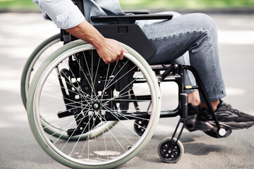 Obraz premium Unrecognizable young black man in wheelchair going for walk in city park, closeup of legs. Cropped view of millennial African American guy with physical disability spending time outdoors