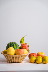 A basket filled with mixed fruits, including apples, placed on a table against a white background, offering a fresh, vibrant display of healthy, natural produce perfect for any setting