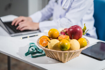 A male nutritionist working at a hospital desk, holding an apple and mixed fruit, offering care, health advice, weight loss guidance, and eating tips online for patients seeking nutrition support