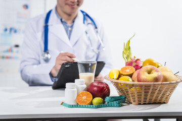 A male nutritionist working at a hospital desk, holding an apple and mixed fruit, offering care,...