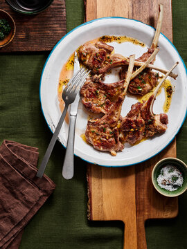 A plate of grilled lamb chops garnished with herbs, served on a wooden board. The meal features tender meat with a hint of seasoning, inviting an appetizing experience