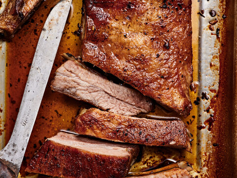 Deliciously cooked brisket rests on a metallic tray, glistening with savory juices. Slices are neatly cut, revealing the flavorful, tender meat perfect for a meal