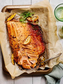 A perfectly baked salmon fillet rests on a baking sheet lined with parchment paper, garnished with lemon slices and scallions. The golden crust is inviting and flavorful