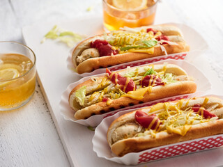 Enjoying flavorful hot dogs placed in white trays, garnished with fresh lettuce, ketchup, and cheese, accompanied by chilled lemonade in glasses during a sunny outdoor event