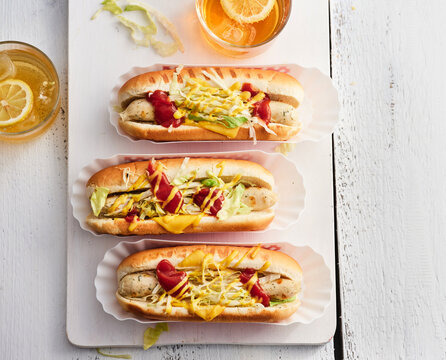 Three tasty hot dogs are garnished with lettuce, mustard, and ketchup, accompanied by cool lemon drinks, ideal for a summer barbecue or picnic setting