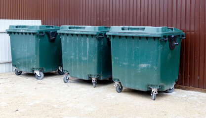 Three green trash cans are lined up against a brown wall