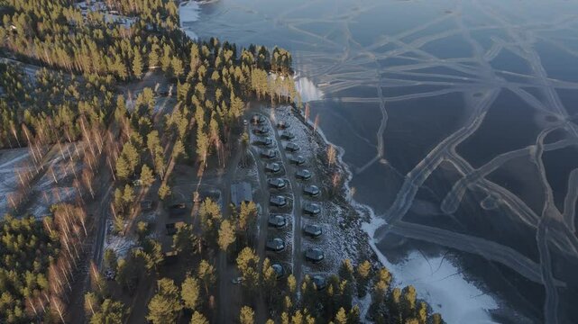 Aerial Tops down Glass Igloos, Eskimo houses around Lapland, Finland forested lake area at Sunset