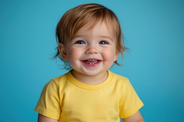 Naklejka premium Cute child smiling in a yellow t-shirt, isolated on blue.