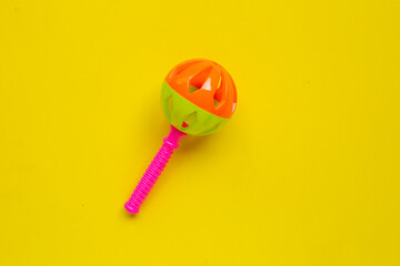 Colorful baby rattles on yellow background. Copy space
