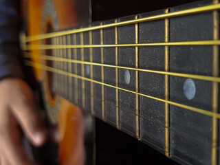Guitar strings in close-up, a hand playing the guitar in the background, a place for text on the side. Guitar lesson. A musical stringed instrument.