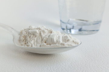 A plastic spoon with protein powder and a glass glass with water on the table. A food protein supplement. Weight gain.