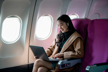 Professional female working on laptop with wireless earbuds during flight commute