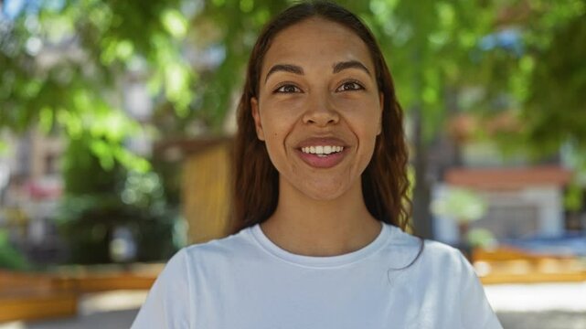 Young woman with a surprised expression standing outdoors in a city park under greenery on a sunny day.