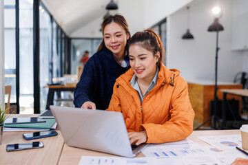 Happy professional women collaborating with enthusiasm in a office setting. Two female entrepreneurs using a laptop for a productive business meeting in a corporate workplace.	
