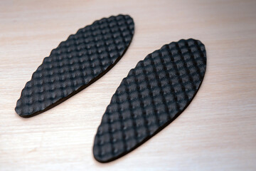 Orthopedic insoles with an uneven black polyurethane surface, displayed on a wooden background. Ideal for promoting foot health and comfort