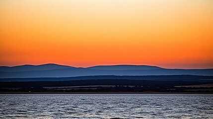 Naklejka premium Golden hour over water and layered hills creating a serene and peaceful landscape scene