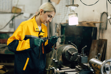 female worker using vernier caliper measuring metal part in lathe machine in heavy metal workshop