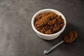 Dark brown granulated sugar in a bowl. Dark background, copy space