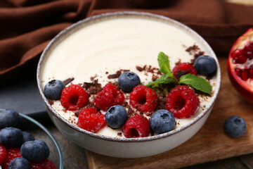Tasty cooked semolina porridge with berries, chocolate and mint on table, closeup