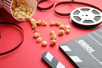 Movie clapper, sweet popcorn and film reel on red background, closeup
