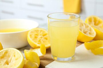 Glass of fresh lemon juice and squeezed fruits on table, closeup