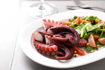 Plate with tasty boiled octopus tentacles and salad on grey table, closeup