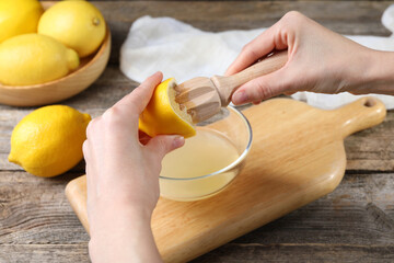 Woman juicing lemon into bowl at wooden table, closeup