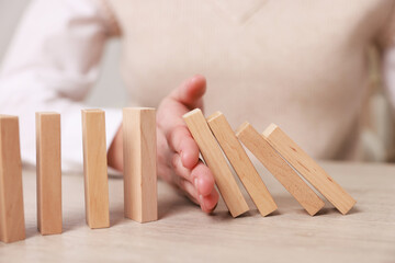 Woman stopping wooden blocks from falling at table, closeup. Domino effect