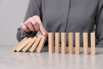 Woman stopping wooden blocks from falling at table, closeup. Domino effect