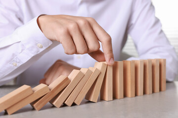 Man stopping wooden blocks from falling at table, closeup. Domino effect