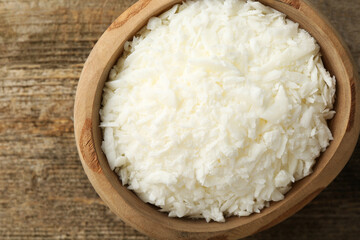 White soy wax flakes in bowl on wooden table, top view