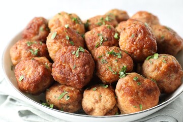 Tasty cooked meatballs with green onion in bowl on white table, closeup