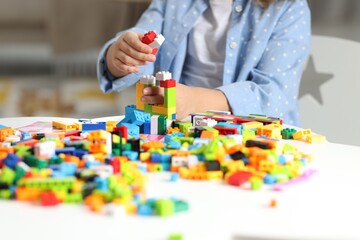 Girl playing with building blocks at white table indoors, closeup