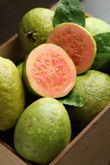 Fresh cut and whole guava fruits in wooden crate on table, closeup