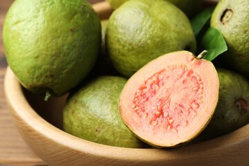 Fresh cut and whole guava fruits in bowl on table, closeup