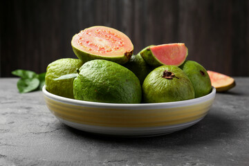 Fresh whole and cut guava fruits in bowl on grey textured table, closeup