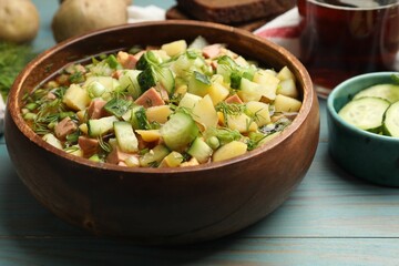 Delicious okroshka soup with kvass and ingredients on blue wooden table, closeup