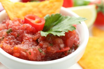 Spicy salsa sauce in bowl and nachos on table, closeup