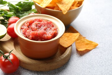 Spicy salsa sauce in bowl, nachos and ingredients on light grey table, closeup. Space for text