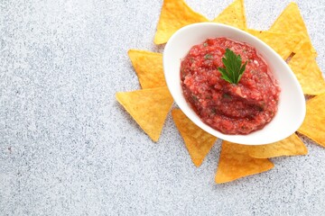 Spicy salsa sauce in gravy boat and nachos on light grey table, flat lay. Space for text