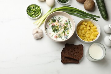Delicious okroshka soup in bowl, garlic, bread and ingredients on white marble table, flat lay. Space for text