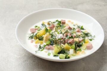 Delicious okroshka soup in bowl on grey textured table, closeup