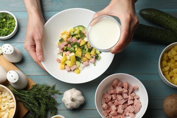 Making okroshka soup. Woman pouring kefir into bowl with different ingredients at light blue wooden table, top view