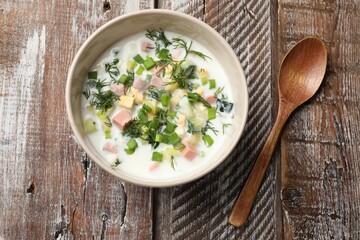Delicious okroshka soup in bowl and spoon on wooden table, top view