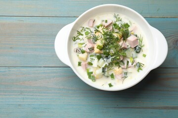 Delicious okroshka soup in bowl on light blue wooden table, top view. Space for text
