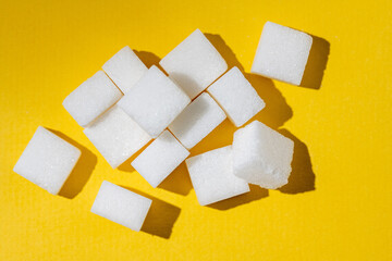 White sugar cubes, isolated on yellow background, hard sun light. Dieting, desserts, overweight,...