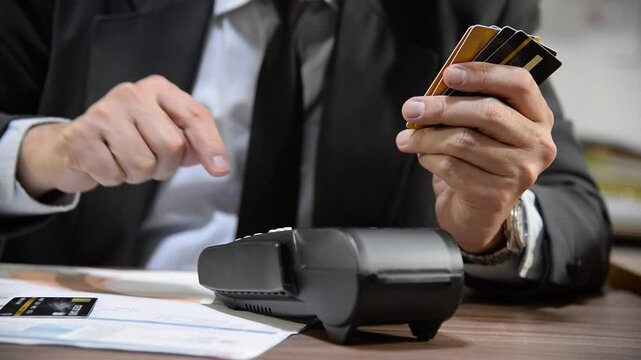 Sad businessman swiping multiple credit cards on a payment terminal at a desk with documents, demonstrating failure financial transactions or corporate expenses management