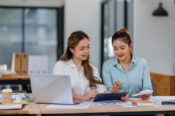 Asian Business women using calculator and laptop for doing math finance on an office desk, tax, report, accounting, statistics, and analytical research concept
